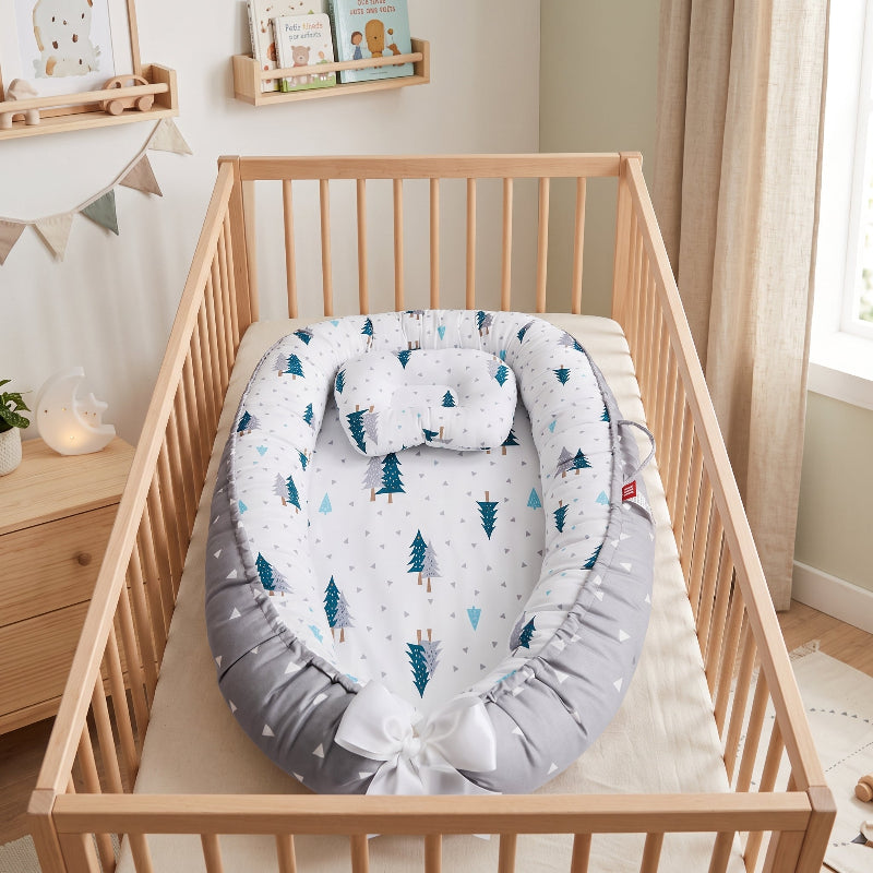 Baby nest à motif sapins posé dans un lit à barreaux