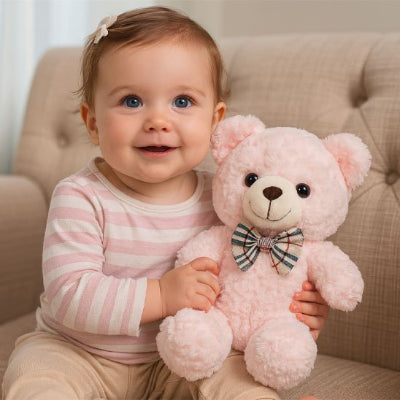 Bébé assis sur un fauteuil tient un ours en peluche rose avec un nœud décoratif.