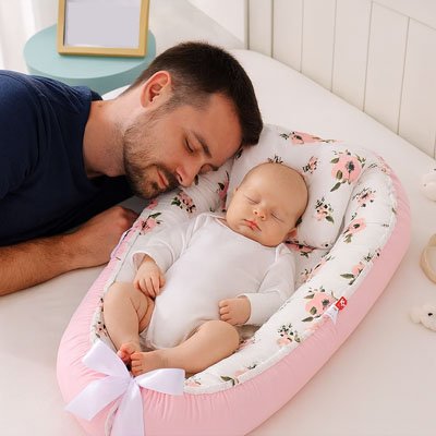 Bébé dort dans un réducteur de lit bébé fleurs roses