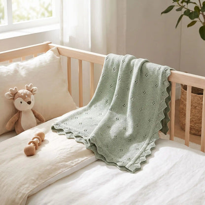 Couverture en tricot bébé vert sauge drapée sur un lit en bois