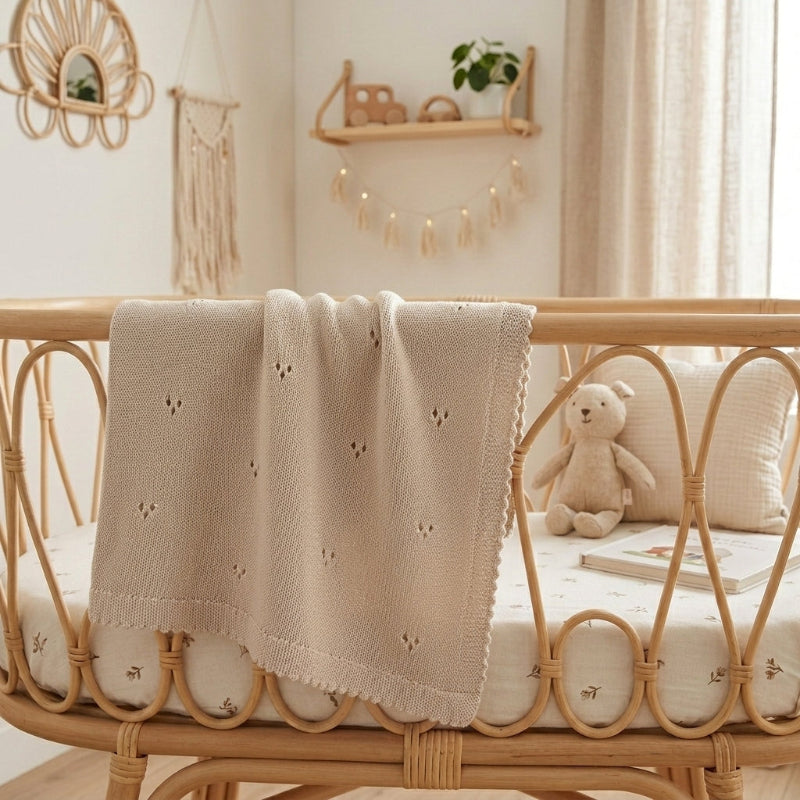 Couverture pour bébé au tricot beige à bord festonné sur un lit