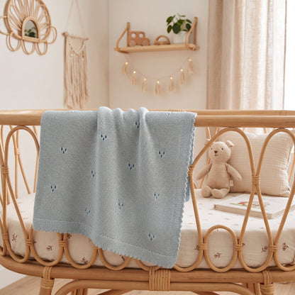 Couverture pour bébé au tricot bleue ajourée sur un lit en rotin