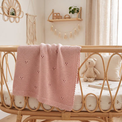 Couverture pour bébé au tricot rose ajourée sur un lit en rotin