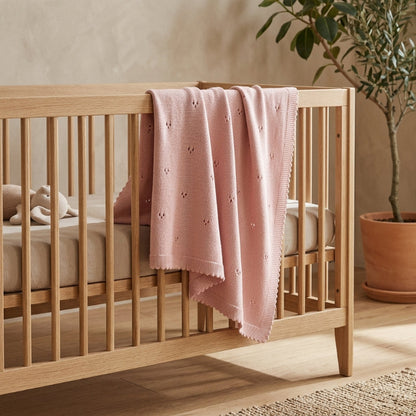 Couverture pour bébé au tricot rose posée sur un lit en bois