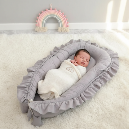 Nouveau-né dormant dans le réducteur de lit respirant gris à volants en coton, posé sur un tapis blanc moelleux avec décoration arc-en-ciel