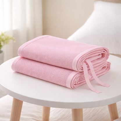 Tour de lit en maille rose plié sur une table