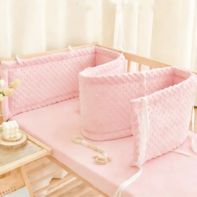 Tour de lit rembourré rose modulable posé le long d'un lit à barreaux en bois