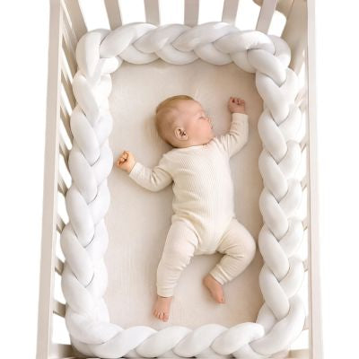 Tour de lit tressé blanc protégeant un bébé pendant son sommeil dans un lit à barreaux