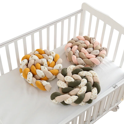 Tresses de lit bébé tressées en plusieurs coloris présentées dans un lit blanc