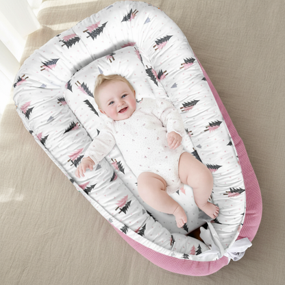 Bébé fille souriante allongée dans le réducteur de lit évolutif motif sapins roses, sur fond naturel lin