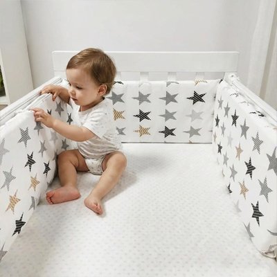 Bébé assis dans son lit entouré d’un tour de lit bébé confortable à motifs