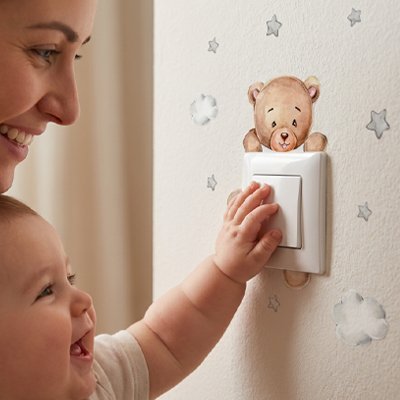 Bébé touchant un interrupteur décoré avec des stickers muraux enfant en forme d'ours.